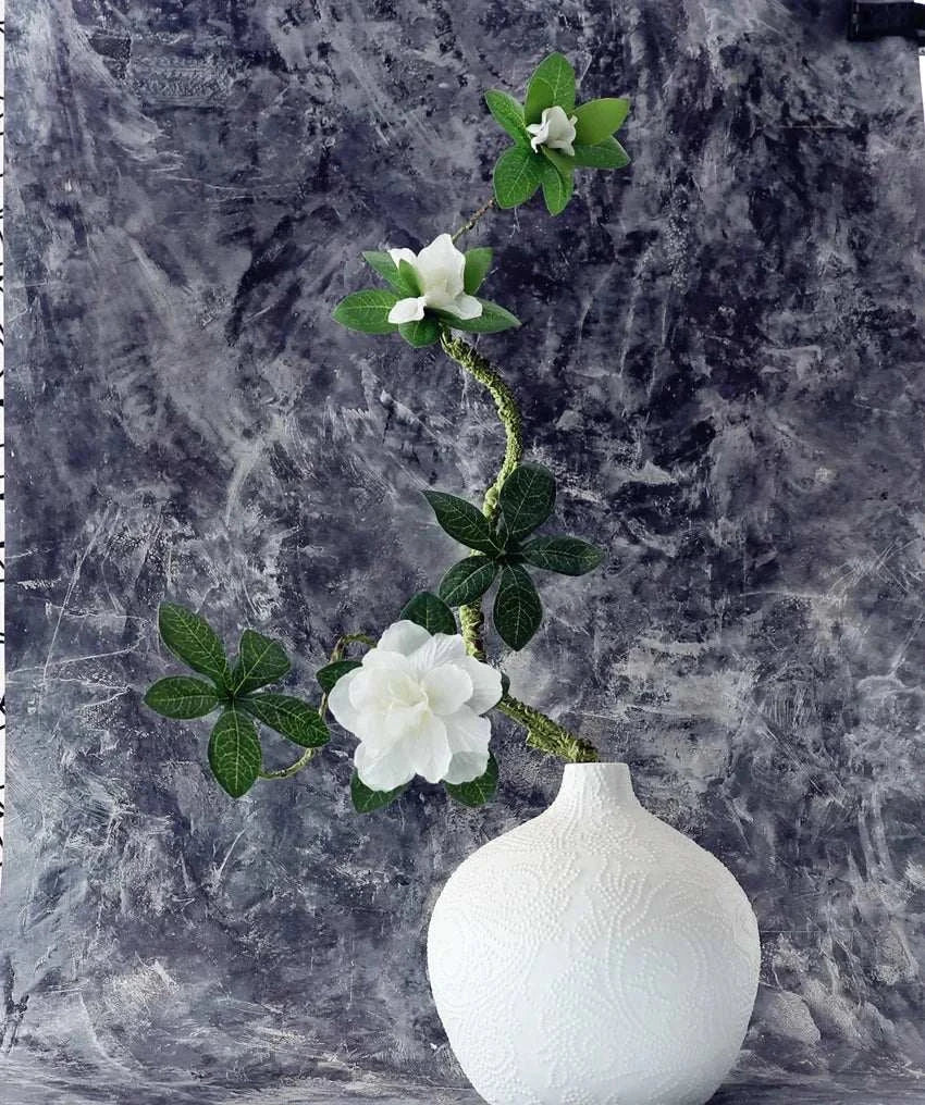 Faux Azaleas Branch in decorative white vase against textured background.