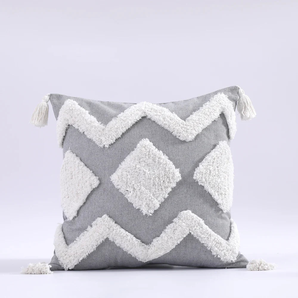 Moroccon style pillow case with intricate white patterns and tassels on a gray background.