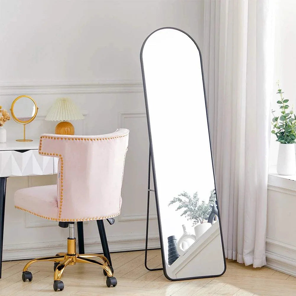 Arched mirror with black metal frame, standing in a stylish room beside a white desk and pink chair.