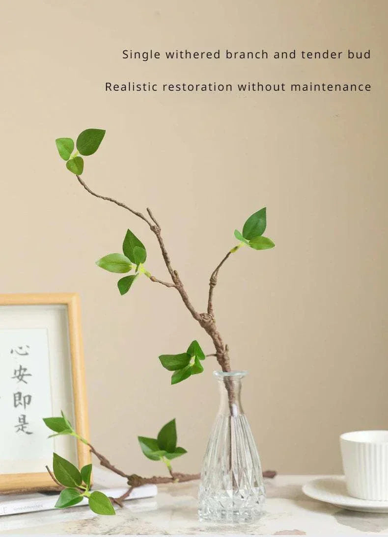 Faux withered branches in a glass vase with green leaves on a table setting.