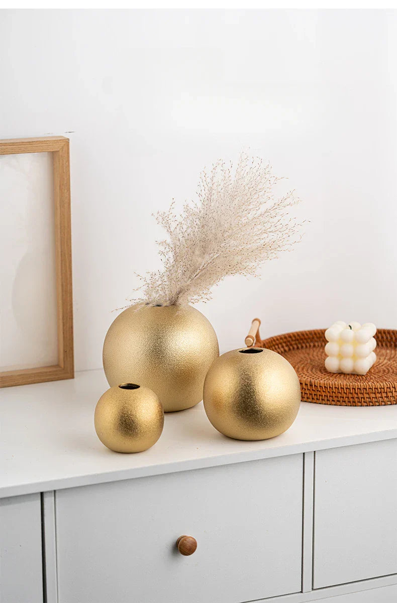 Nuala Ceramic Balls in gold finish as vases on a white cabinet with a decorative arrangement.