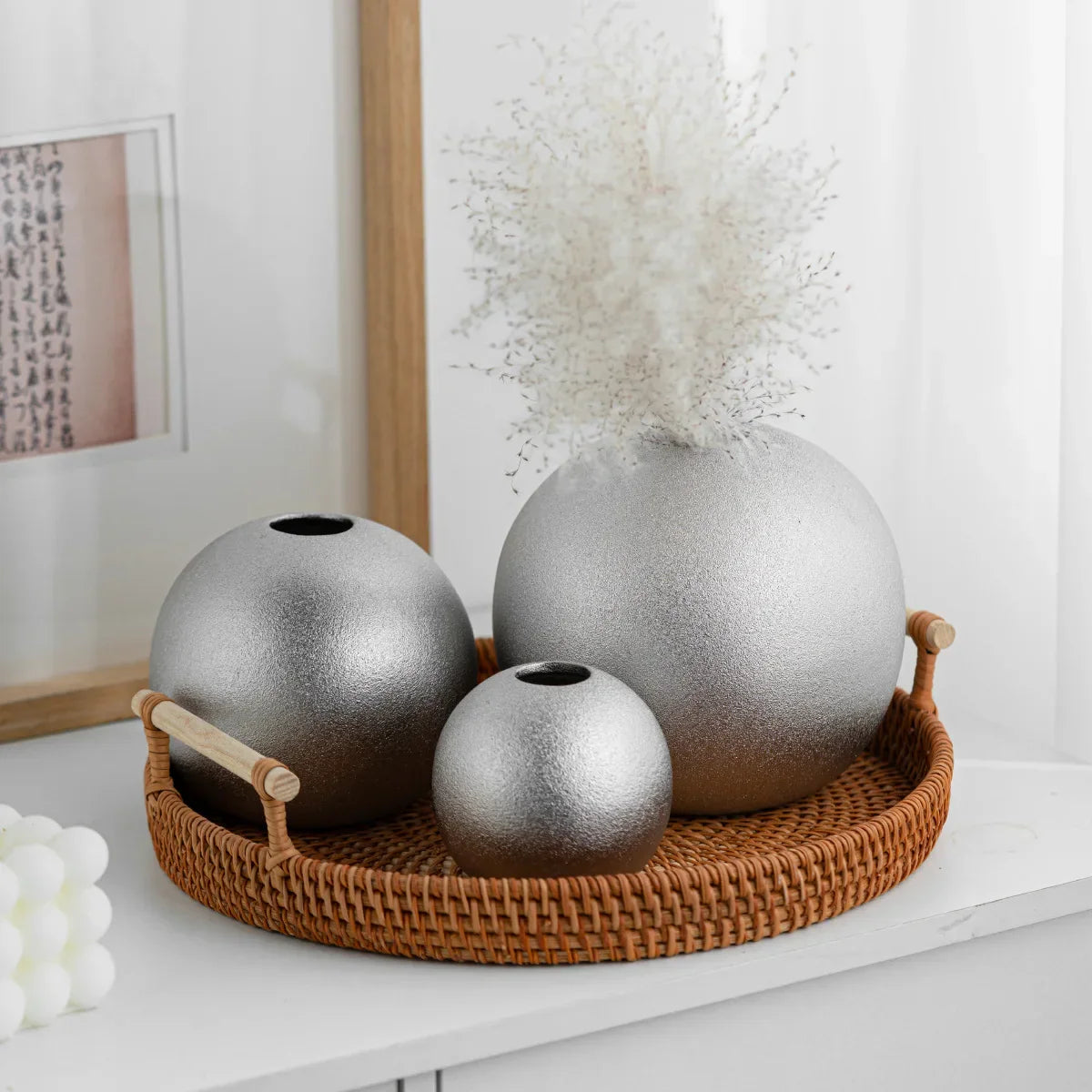 Nuala Ceramic Balls in silver on a wicker tray serving as decorative ornaments or vases, adding elegance to a room setting.