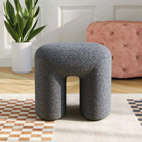 Grey Theadra Ottoman in teddy bear fur upholstery, versatile as footrest or seating, in stylish living room setting.